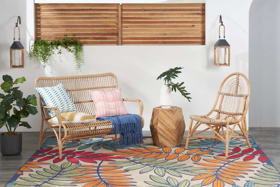 Nourison tropical area rug on porch with rattan furniture and bright accent pillows